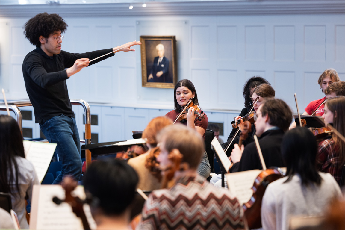 A male conductor leading an orchestra rehearsal.